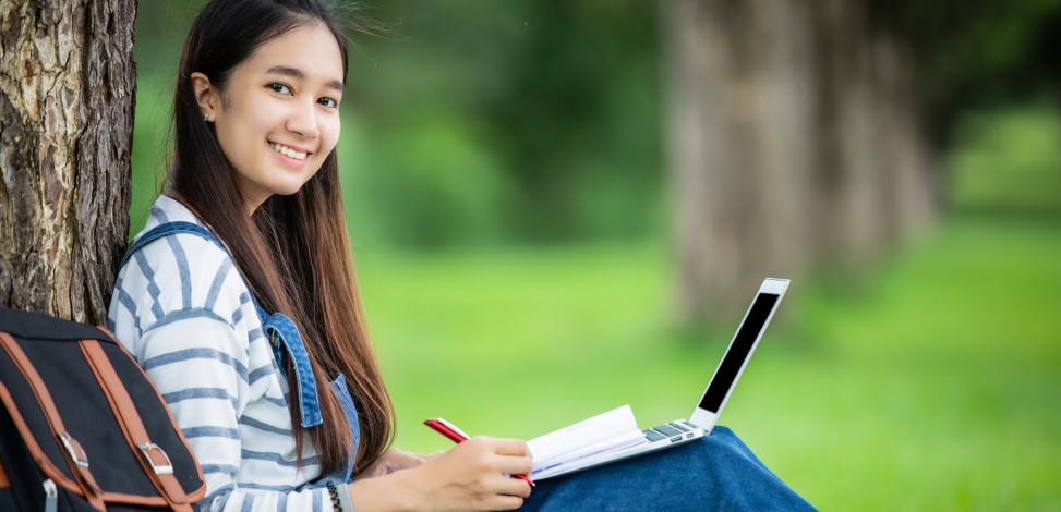 A college student sits in a park working on a project.