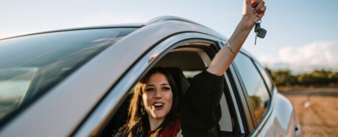 A teen celebrates her first car as she holds her keys triumphantly out the driver’s side window.