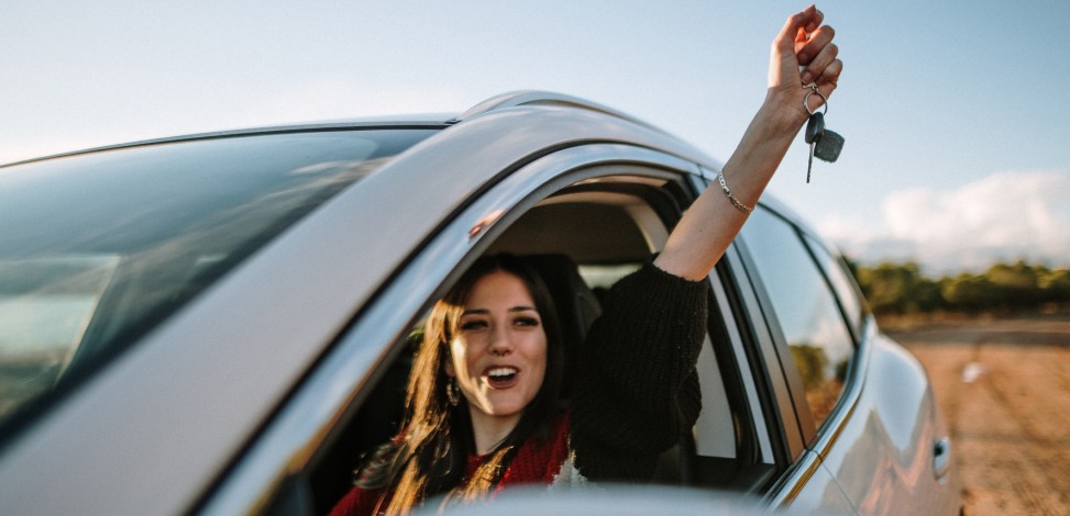 A teen celebrates her first car as she holds her keys triumphantly out the driver’s side window.