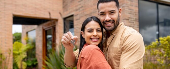 A Latino couple hugs with the keys to their new home.