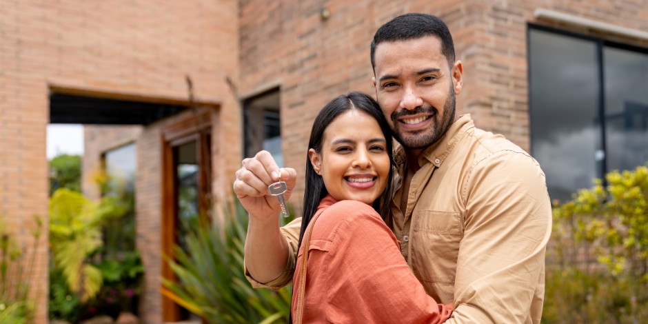 A Latino couple hugs with the keys to their new home.