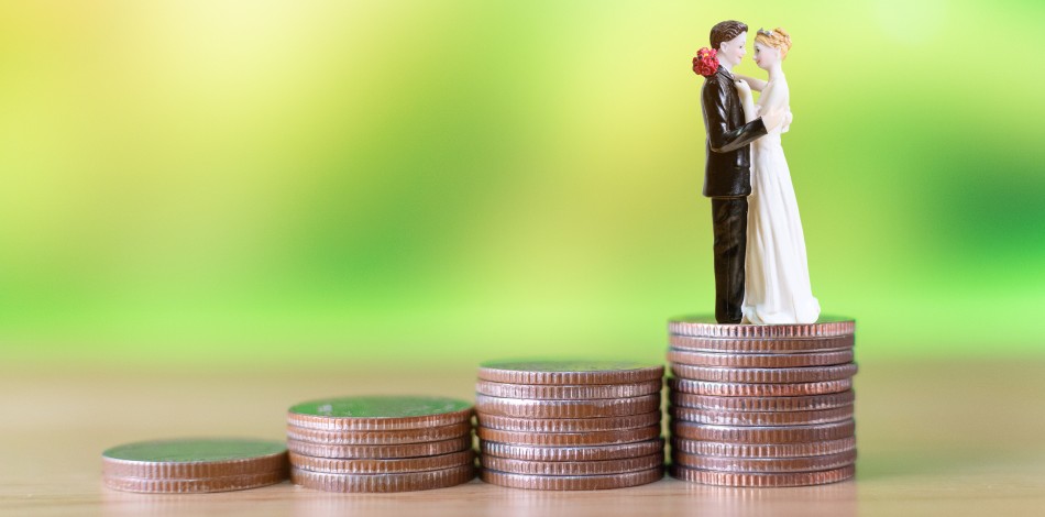 A toy bride and groom stand atop a pile of coins